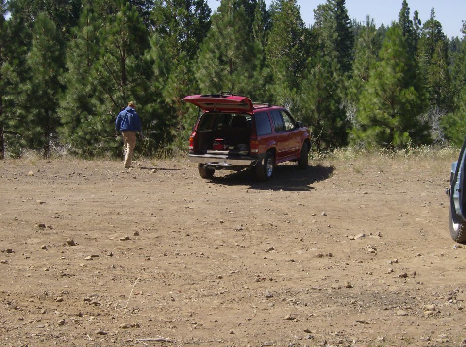 Red SUV with open hatch parked on dirt road near trees, person walking away.