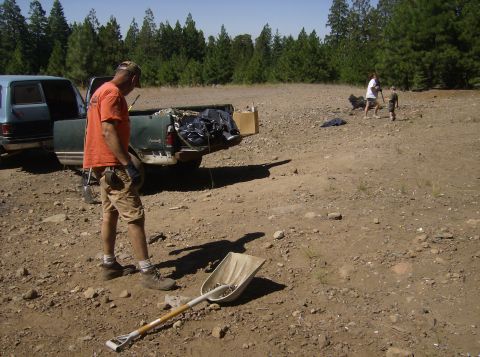 1986 Ford Bronco - A man wearing an orange t-shirt and tan shorts stands near the back of a green pickup truck. A shovel is lying on the ground in the foregro…
