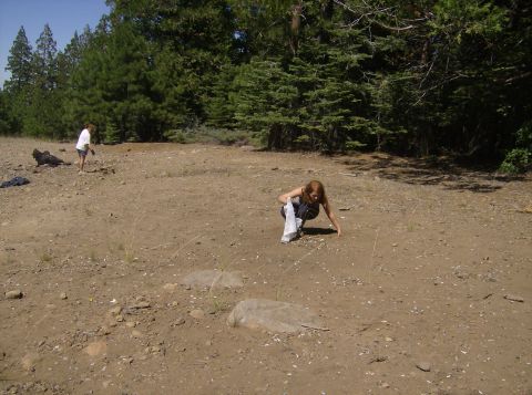 1986 Ford Bronco - Two people are in a dry, dusty clearing with trees in the background. One person is standing and the other is crouching.