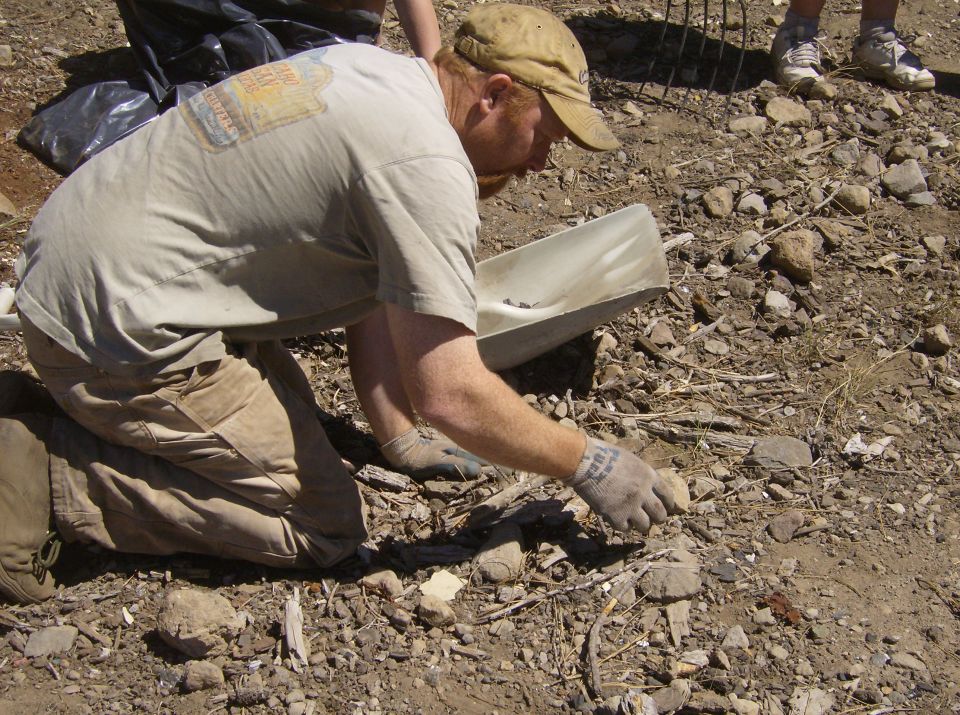 Person kneeling on the ground examining rocks and debris with a scoop.