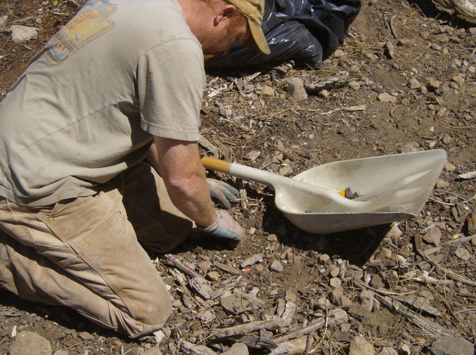 Person kneeling by a shovel with debris.