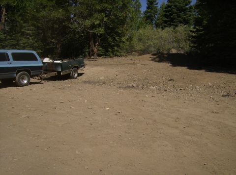 1986 Ford Bronco - A blue SUV is parked on a dirt road, hitched to a green trailer. The trailer contains some white objects and appears to be a converted pick…