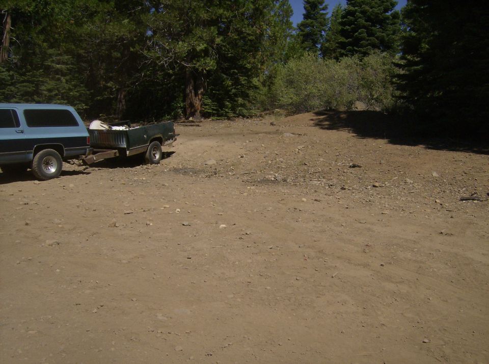 Blue SUV towing a green trailer on a dirt road near trees.