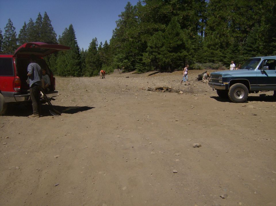 Blue pickup truck parked on dirt lot with trees, red SUV with open hatch to the left.