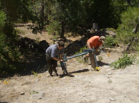 1986 Ford Bronco - Two people are working on a metal contraption in a wooded area. One person is wearing a striped shirt and the other is wearing an orange sh…
