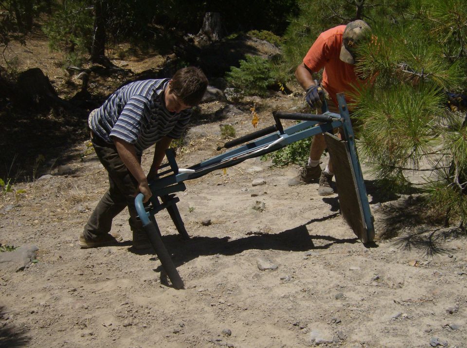 Two people working on a blue and black metal contraption outdoors.
