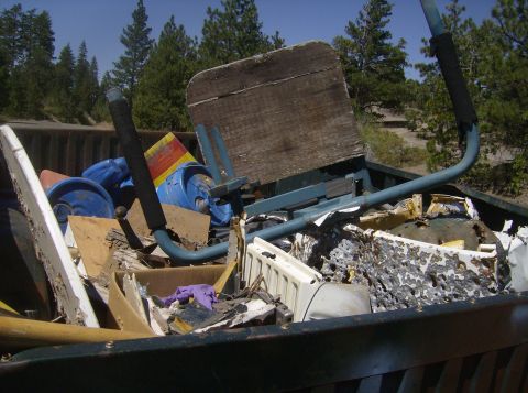 1986 Ford Bronco - A close-up view of the bed of a pickup truck filled with various debris, including blue plastic containers, wooden planks, and a metal fram…