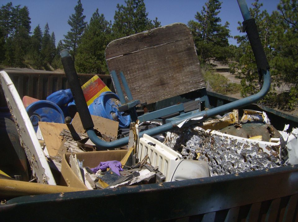 Debris in a pickup truck bed, including blue containers and a metal frame with a wooden seat.