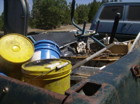 1986 Ford Bronco - The bed of a pickup truck is filled with various items including yellow and blue buckets, a blue van in the background, and other miscellan…
