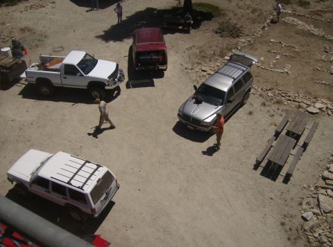 1986 Ford Bronco - An overhead view shows a silver SUV with its rear hatch open, parked on a dirt lot next to a wooden picnic table. A person in an orange shi…