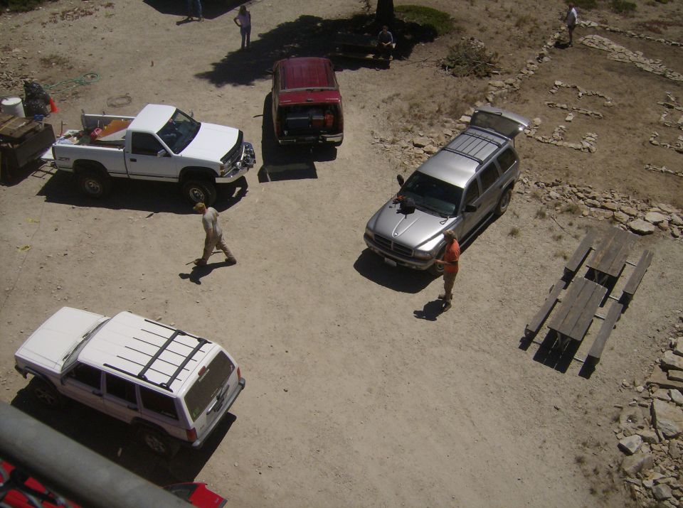Silver SUV with open hatch parked on dirt lot next to picnic table, person standing nearby.