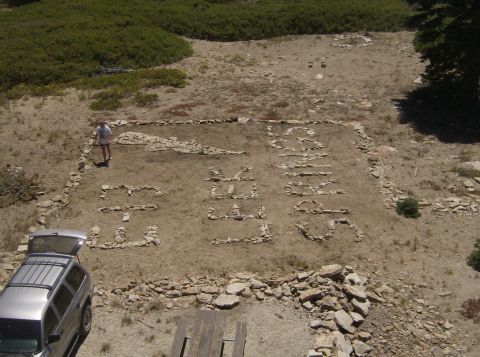 1986 Ford Bronco - An aerial view shows a silver SUV parked next to a large stone arrangement spelling out "GO SEEK" on a dirt ground. A person stands near th…