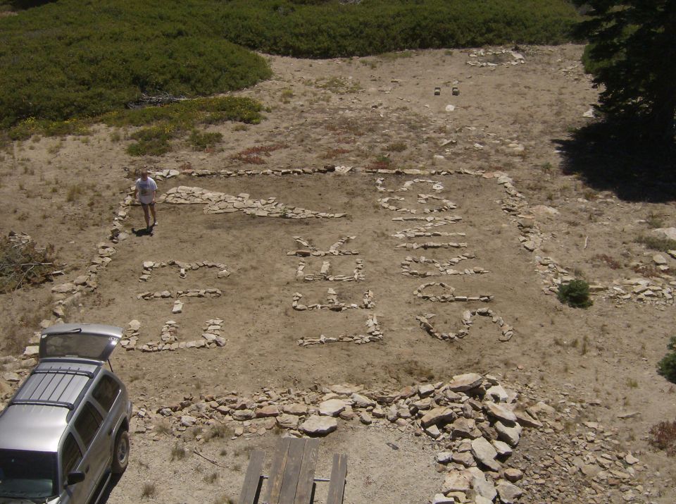 Silver SUV parked next to stone letters spelling "GO SEEK" on dirt ground.
