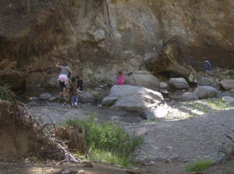 1986 Ford Bronco - A group of children and an adult are exploring a rocky creek bed near a steep, eroded embankment.