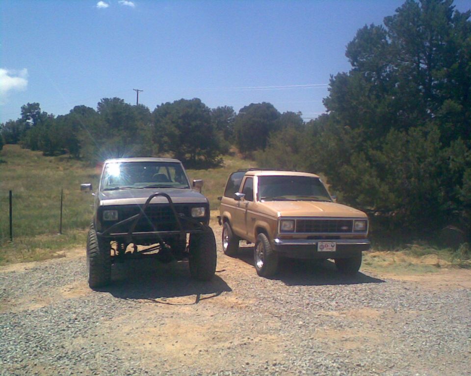 Two Ford Bronco II SUVs parked on a gravel lot with trees in the background.