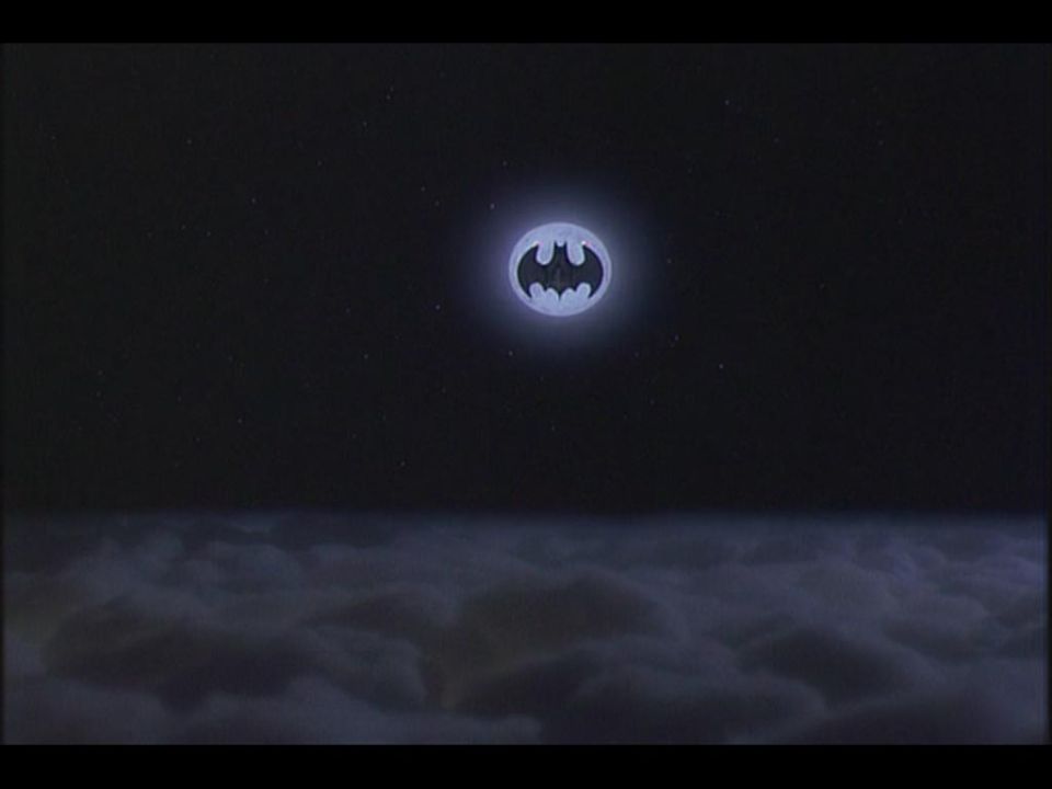 A glowing Batman symbol in the night sky above clouds.