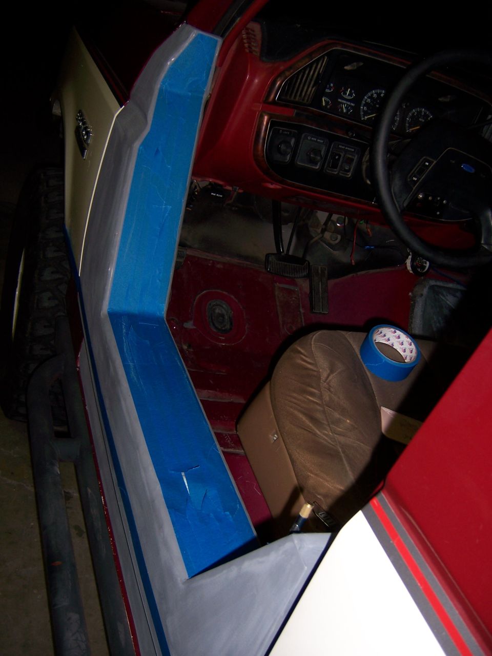 Interior of a 1991 Ford Bronco showing the driver's side door panel and dashboard. The door panel is being worked on, with blue tape visible