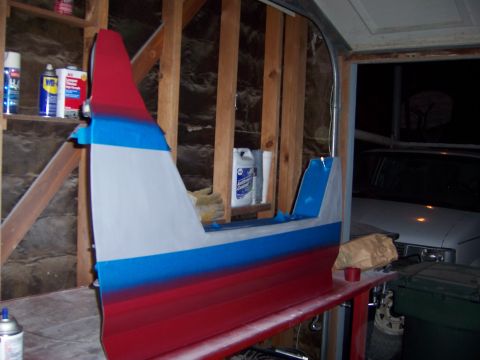 1991 Ford Bronco - A vehicle door, in the process of being painted with red, blue, and white stripes, rests on a workbench in a garage.