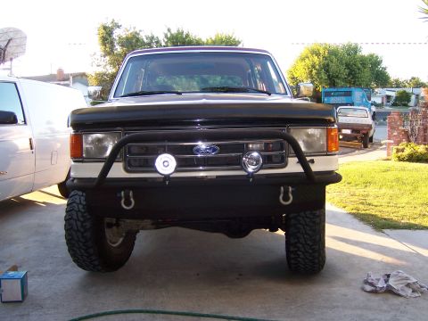 1991 Ford Bronco - A white and black Ford Bronco is parked in a driveway, showing its front grille and bumper.