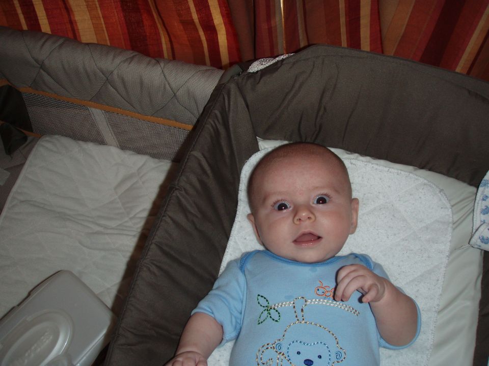 Baby in a blue onesie with a monkey design lying in a crib.