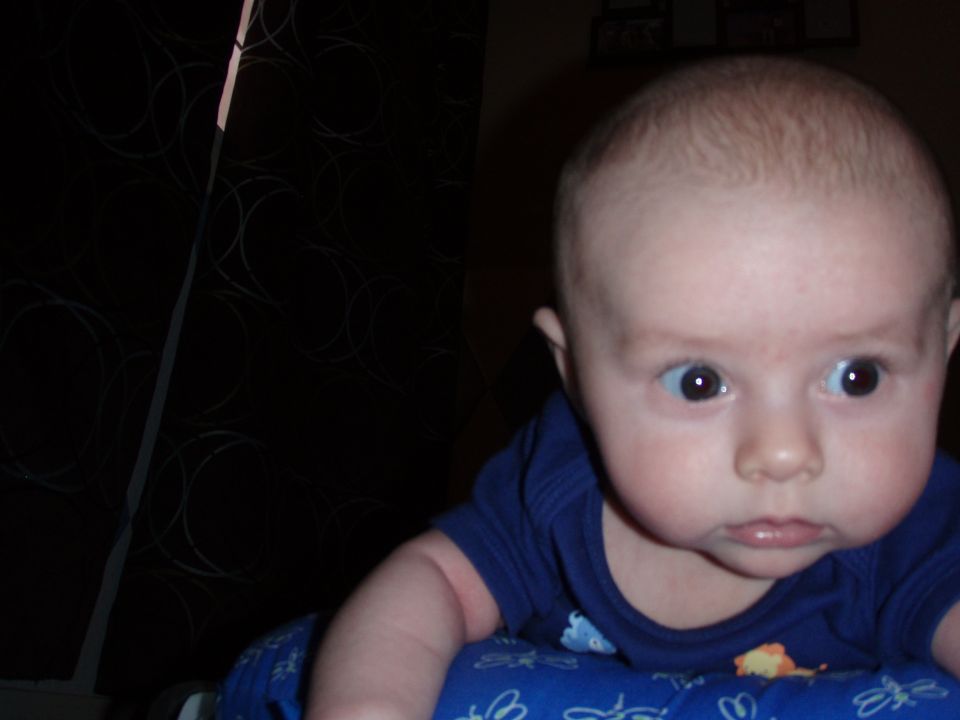 Close-up of a baby's face wearing a blue shirt, looking up and to the side.