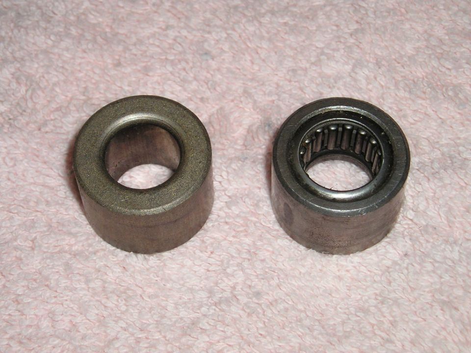 two cylindrical metal parts, one with visible rollers inside, on a pink fabric surface
