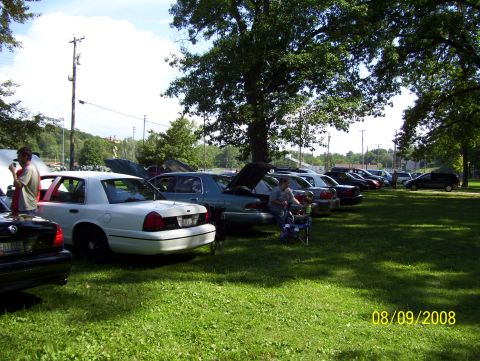 2008 Ford Crown Victoria - A line of cars are parked on a grassy field under trees, with a date stamp of 08/09/2008.