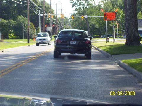 2008 Ford Crown Victoria - A black sedan is seen from behind on a suburban street, with another white SUV ahead.