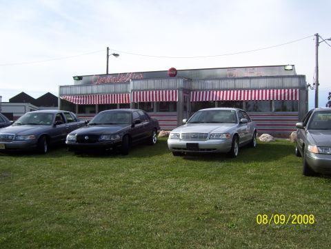 2008 Ford Crown Victoria - Several Ford Crown Victorias are parked on the grass in front of a diner with red and white striped awnings.