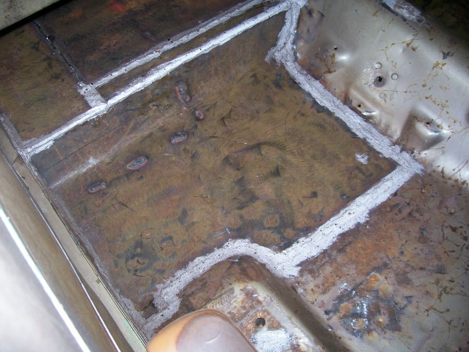 Rusted metal floor pan with white sealant applied in a geometric pattern