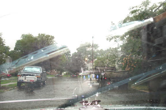 Rainy street seen through a windshield with wipers and a parked pickup