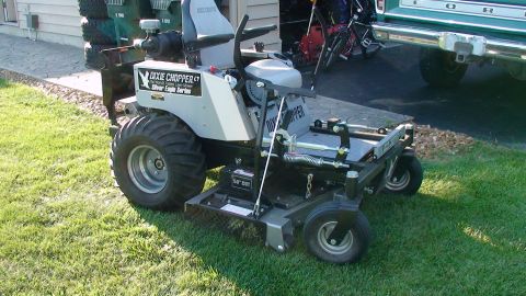 1979 Ford Bronco - A Dixie Chopper zero-turn mower with large rear tires is shown on a lawn next to a building and a pickup truck.