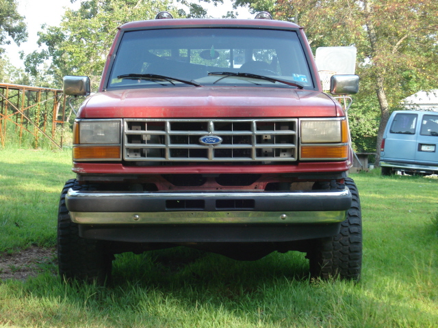 Red Ford SUV front view, lifted suspension, chrome bumper, grille with Ford logo, off-road tires