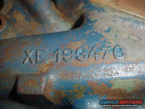 Close-up of a blue, rusty metal engine part with stamped numbers XE 193476 and XD7A6 9424 HR
