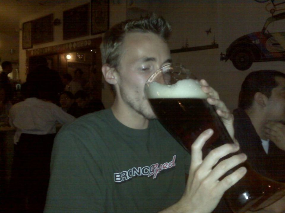 Man in green t-shirt with "BRONCOspeed" text drinks from a very large beer glass