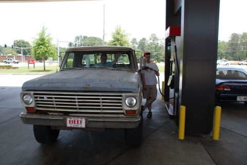 1996 Ford Bronco - A man pumps gas into a vintage Ford pickup truck at a station.
