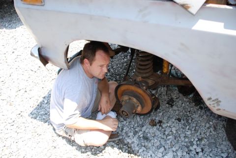 1996 Ford Bronco - A man inspects the suspension system of a vehicle, focusing on the brake rotor and coil spring.