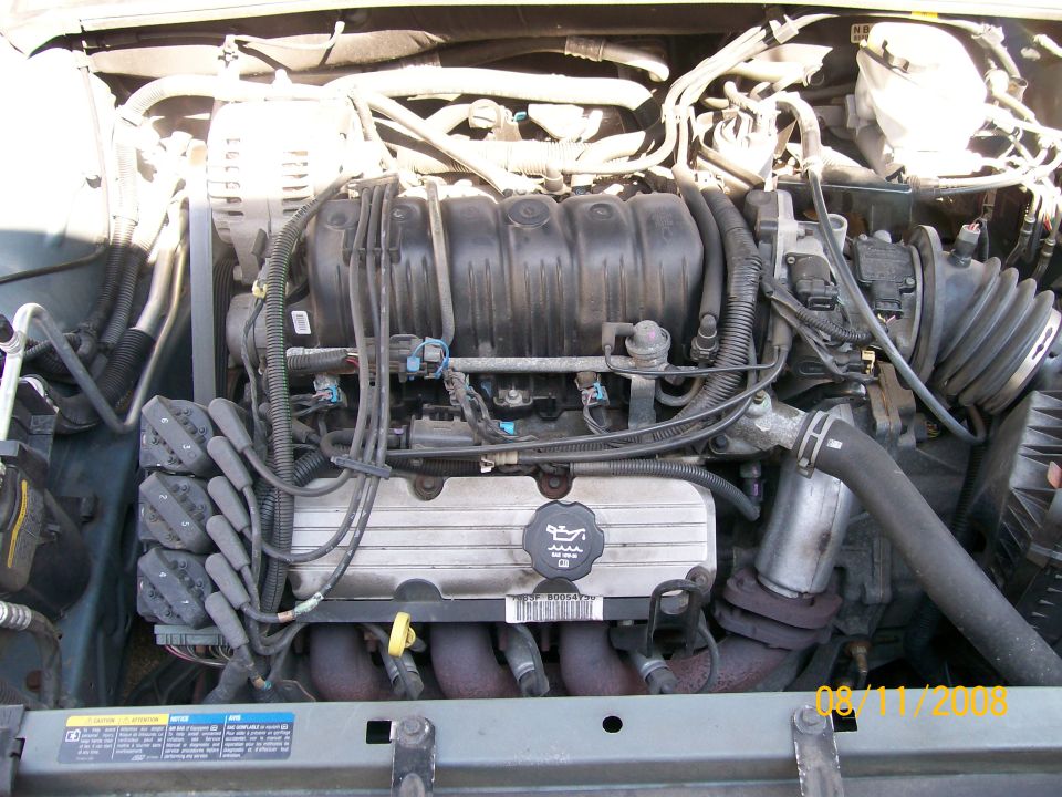 Engine bay with V6 engine components visible, including spark plug wires, intake manifold, and alternator
