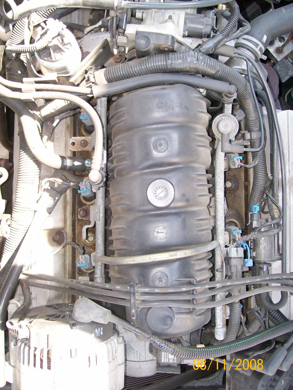 Close-up of a car's engine bay, showing hoses, wires, and the intake manifold