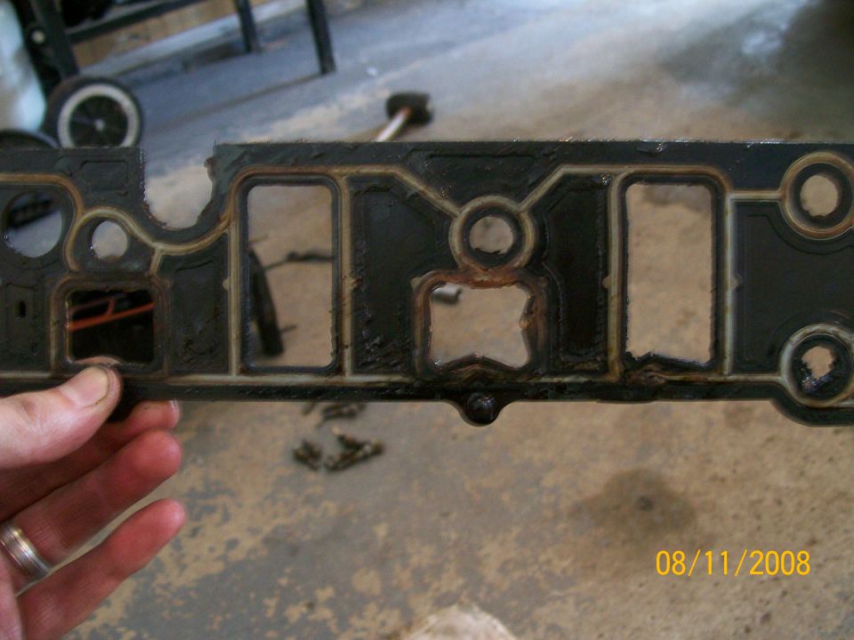 Hand holding a used intake manifold gasket with multiple openings