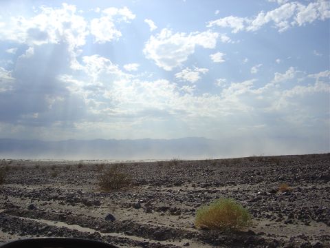 2001 Ford Mustang - A wide shot of a dry, rocky desert landscape with mountains on the horizon and a cloudy sky above.