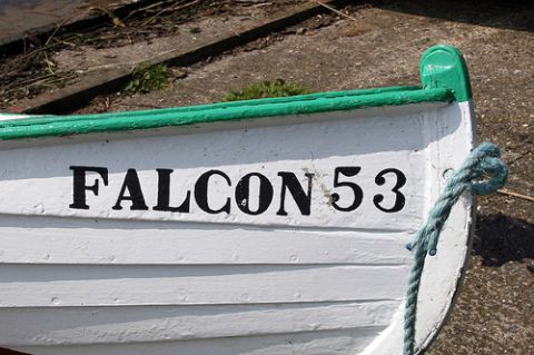 1992 Ford Bronco - The bow of a white and green watercraft is visible, with the name "FALCON 53" painted in black on its side. A blue rope is tied to the fron…