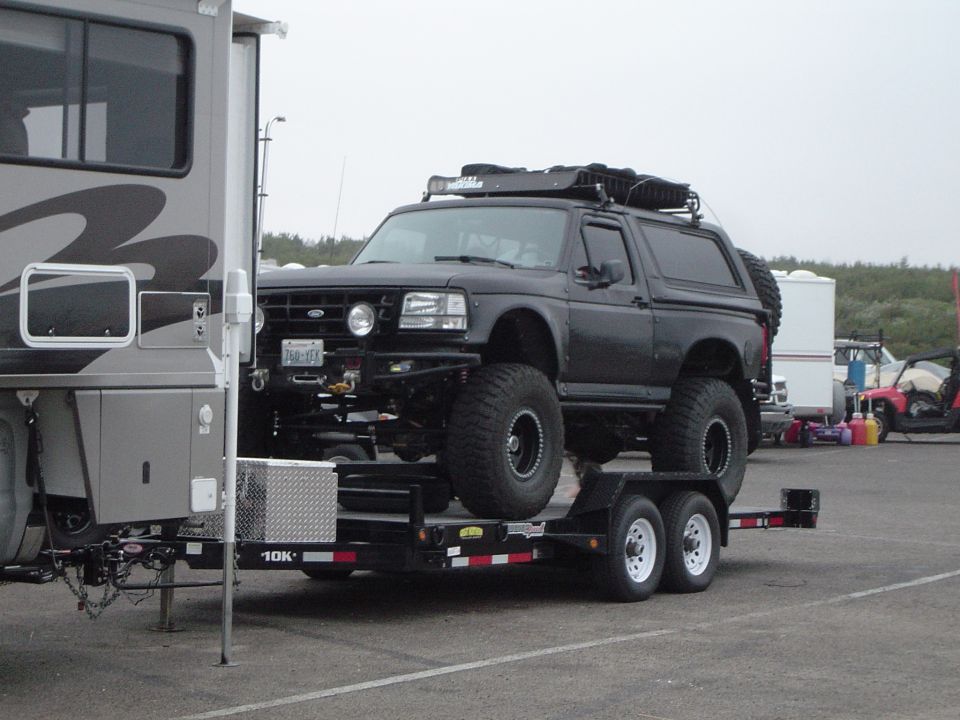 Black lifted Ford Bronco loaded on a flatbed trailer behind an RV