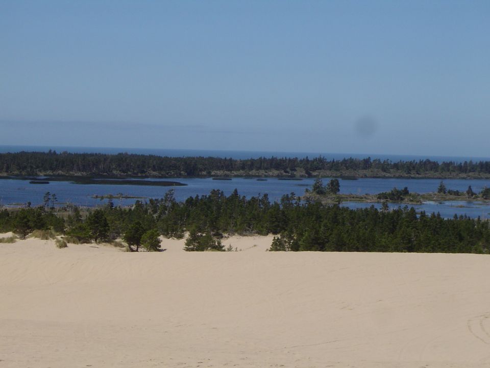 Sand dune overlooking a lake, forest and ocean under a clear sky