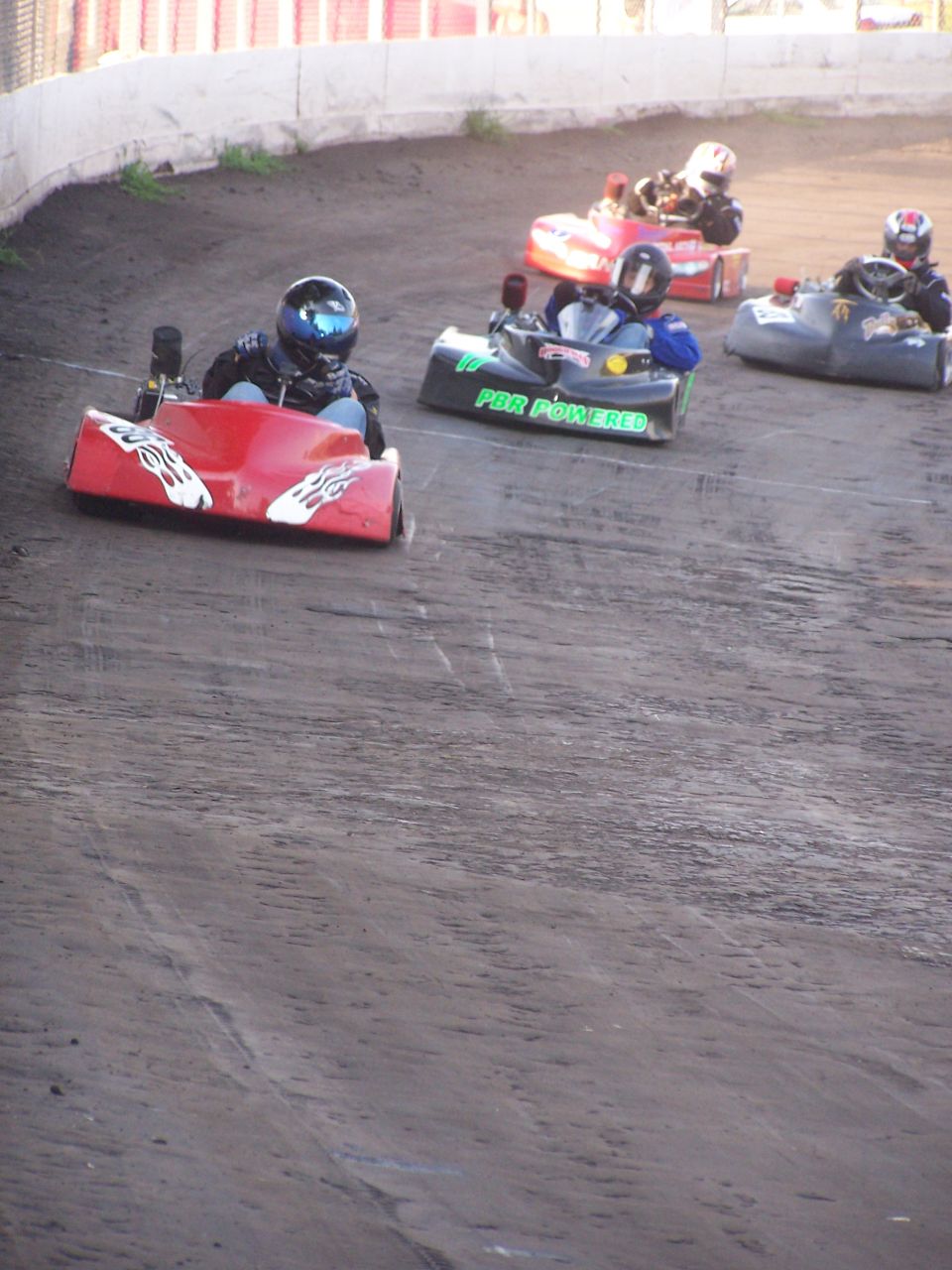Go-karts racing on a dirt track, one red kart in front with flames.