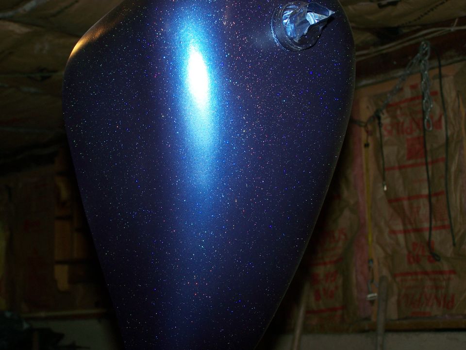 Dark blue metalflake teardrop motorcycle fuel tank hanging in a shop