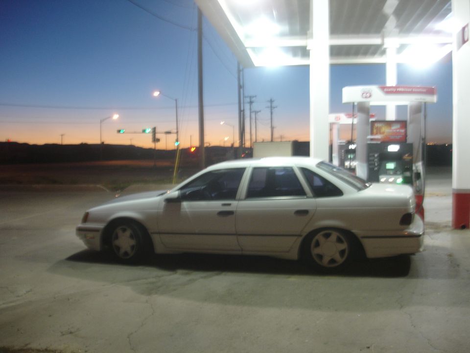 White four-door sedan parked at a gas station at dusk.