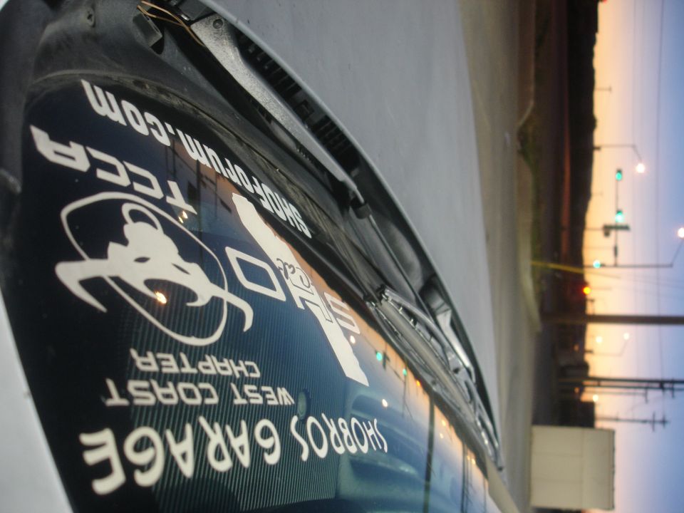White stickers on a vehicle's rear window: SHOPFORUM.COM, TCCA, West Coast Chapter, Shorros Garage.