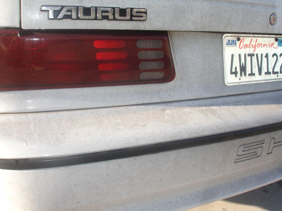 Rear view of a dusty white 1990 Ford Taurus with a California license plate.