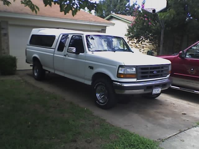 White 1990s Ford F-150 pickup truck with a camper shell, parked in a driveway.